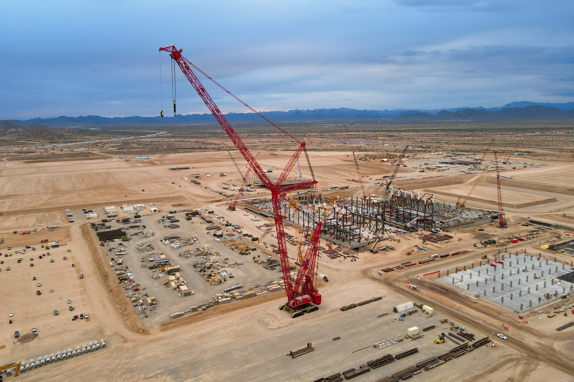 Aerial view of an industrial gas plant construction site with steel structural framing, large crawler crane, and desert terrain