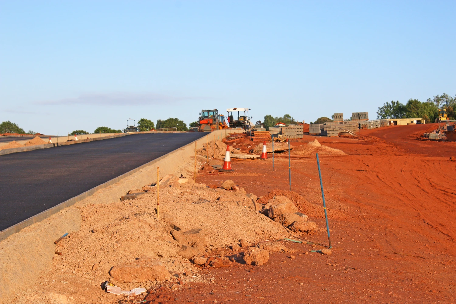 New road construction site showing graded subgrade, road base, and heavy equipment paving the surface