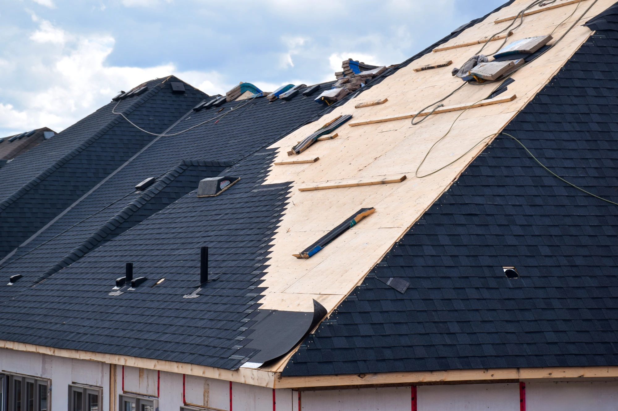 : Close-up of shingle roof installation showing plywood decking, underlayment, and new shingles being applied